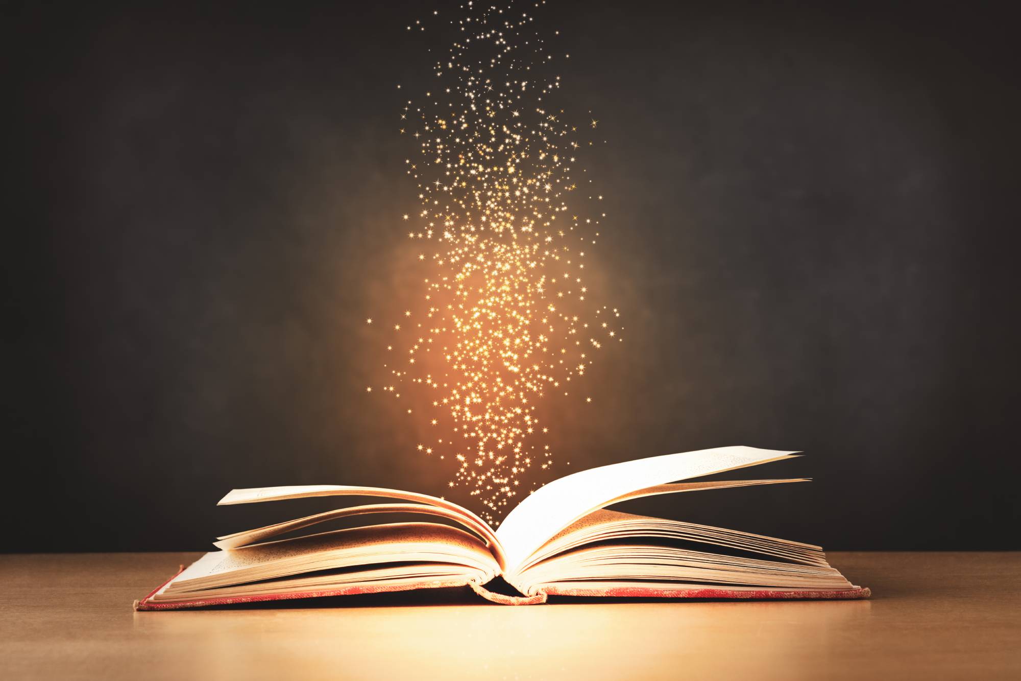 An old, worn, red text book, lying opened on a classroom desk with sparkles and stars rising upwards from its centre. Black chalkboard background. An old, worn, red text book, lying opened on a classroom desk with sparkles and stars rising upwards from its centre. Black chalkboard background.