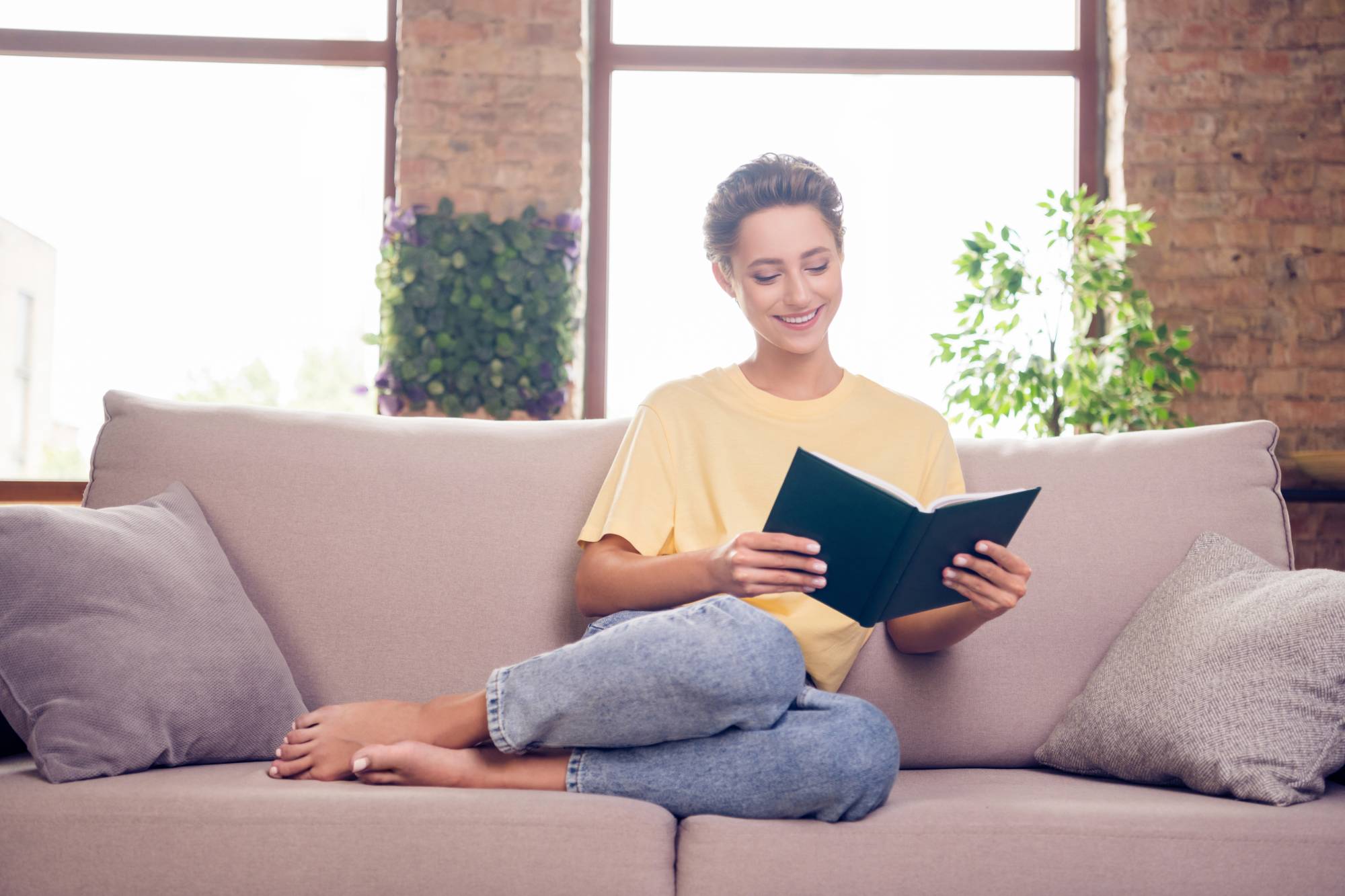Full length photo of cheerful young positive pretty woman sit sofa read book smile indoors inside house home Full length photo of cheerful young positive pretty woman sit sofa read book smile indoors inside house home